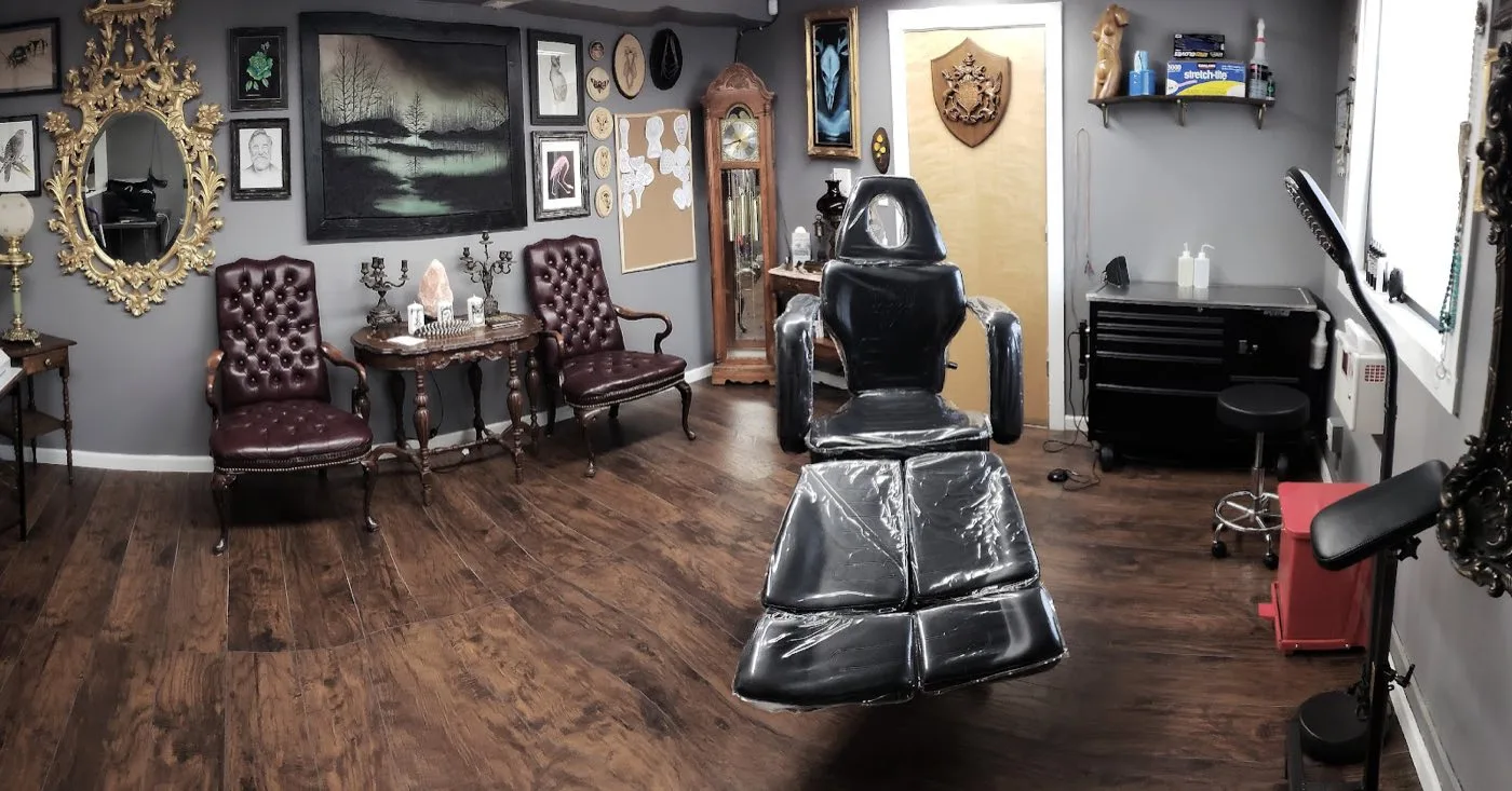 A tattoo room with a black client chair, Victorian armchairs, framed art and a gold mirror